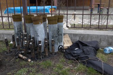 Sayılar ve daha küçük mermi parçalarıyla işaretlenmiş birkaç büyük silindirik kovan da dahil olmak üzere çeşitli mühimmatlar bir çitin yanında yerde yatıyor.