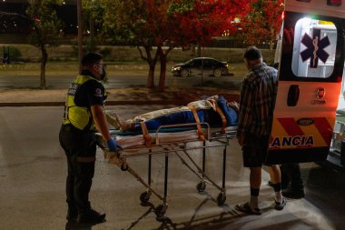 Bir insan sedyede yatar ve gece ambulansın arkasına yüklenir.