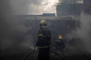 İtfaiyeciler dumanla dolu bir şehirde yanan bir otobüsle uğraşıyorlar.