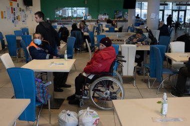 Several individuals are present in a well-lit indoor area with tables and chairs