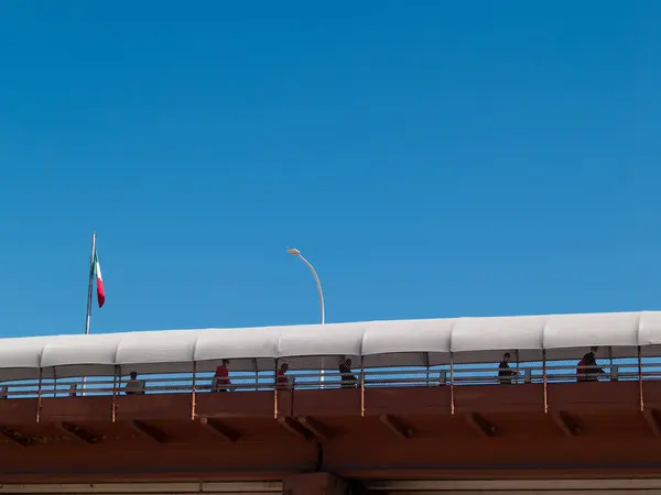 Göçmen siluetleri uluslararası bir köprüden geçerek ABD-Meksika sınırına giriyor.