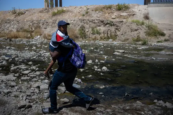 Bir adam yürürken omzunda kırmızı beyaz bir giysi taşıyan küçük bir çocuk taşıyor.