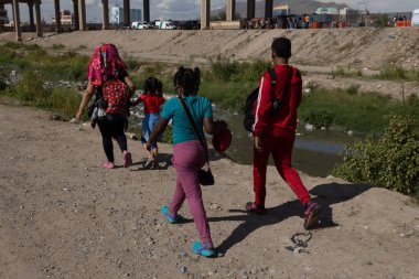 Göçmen bir aile, bölgede devam eden göç sorunları arasında, uluslararası bir sınır kapısına yaklaşan nehir kıyısındaki kirli bir patikada yürüyor.