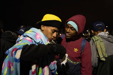 A group of migrants wrapped in blankets and warm clothes gather outdoors at night in an improvised camp in Ciudad Jurez, Chihuahua, near the U.S.-Mexico border