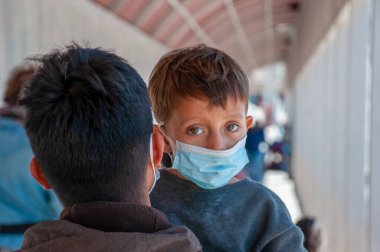 Açık mavi tek kullanımlık maske takan genç bir çocuk Ciudad Jurez, Chihuahua, Paso del Norte uluslararası köprüsüne sınır dışı edildikten sonra doğrudan kameraya bakıyor.