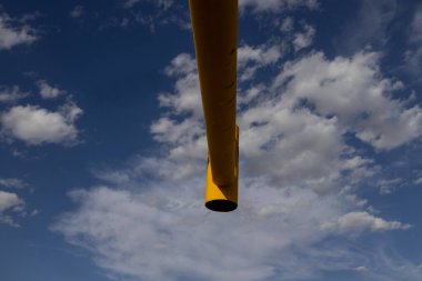 Parlak mavi gökyüzüne çarpan sarı bir direğin alçak açılı görüntüsü, şehir manzaralarında kentsel tasarımın doğayla olan parlak zıtlığını simgeliyor..