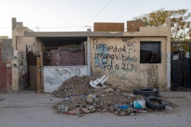 İhmal edilmiş bir şehir binası. Grafiti ile işaretlenmiş ve etrafı lastik ve kırık mobilya gibi çöplerle çevrili. Kentsel bozulma sorunlarını vurguluyor..