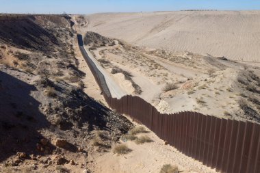 Ciudad Juarez yakınlarındaki çorak sınır manzarası, uzun çit ve toprak yollarla işaretlenmiş, göç politikasındaki gerginliği yansıtıyor..
