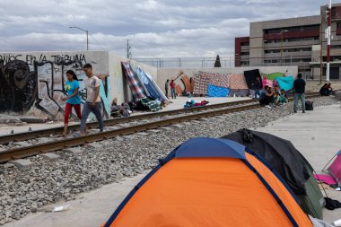 Göçmenler, sürmekte olan göç krizleri sırasında Ciudad Juarez sınırındaki geçici yerleşim sorunlarının altını çizerek, geçici barınaklar yakınlarındaki demiryolu boyunca yürüyorlar..