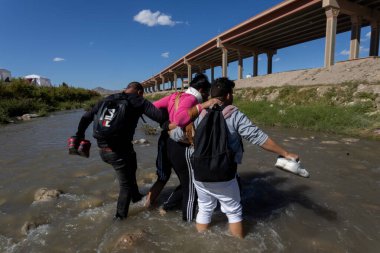 Göçmenler, ABD 'ye doğru yol alırken üzerinde eşyalar bulunan Ciudad Juarez köprüsünün altından geçen bir nehri geçerek, devam eden sınır sorunları ve insani sorunların altını çiziyor..