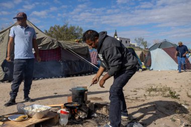 Göçmenler, ABD-Meksika sınırını geçmek isteyenlerin karşı karşıya kaldıkları zorlu koşulları yansıtan Ciudad Juarez 'deki geçici bir kampta yemek hazırlıyorlar..
