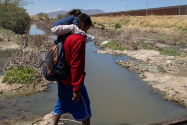 Ciudad Juarez 'deki yüksek sınır çitlerinin yanında çocuk taşıyan bir adam..