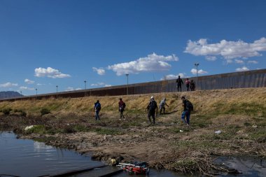 Göçmenler yüksek Ciudad Juarez sınır çitinin oradaki engebeli araziden geçiyorlar..