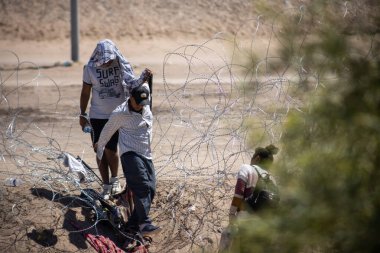 Göçmenler Ciudad Juarez yakınlarındaki dikenli tellerde geziniyorlar, gerekli şeyleri taşıyorlar..