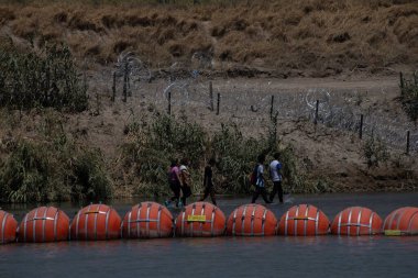 Göçmenler Ciudad Juarez 'deki su bariyerlerinin yanında dikenli tellerin yanından geçiyorlar..