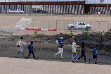 Göçmenler Ciudad Juarez 'deki tahkim edilmiş sınır çitlerinin oradaki çamurlu arazide geziniyorlar..