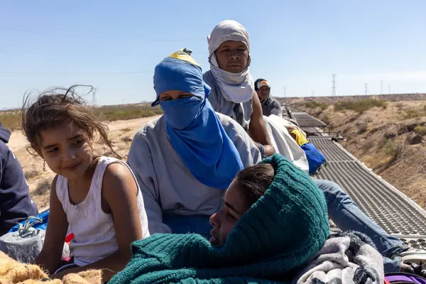Ciudad Juarez yakınlarındaki seyrek çöl arazisinden geçen düz bir yük treninin tepesinde bir aile, düzensiz bir geçiş için Rio Grande 'ye yaklaşıyor..