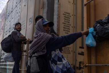 Ciudad Juarez yakınlarındaki bir yük trenine tutunan üç göçmen Birleşik Devletler sınırına doğru yola çıkmaya hazırlar..