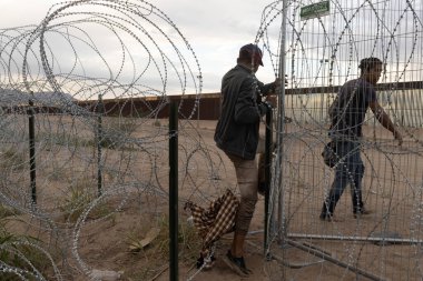 İki göçmen, Ciudad Juarez sınırındaki güçlendirilmiş dikenli telleri aşıyor. Göç sorunları için önemli bir nokta..