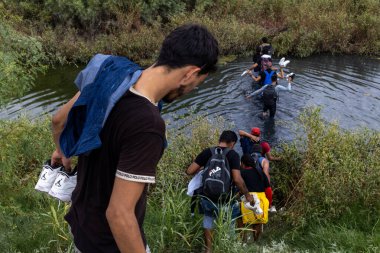 Ciudad Juarez nehrindeki göçmenler, yoğun yeşilliklerin ortasında eşyalarla dolu..