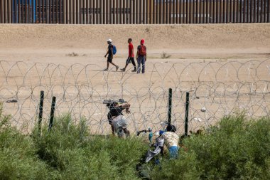 Ciudad Juarez 'deki yüksek sınır çitlerinin yanından geçen üç göçmen, dikenli tellerin yanında dinlenirken, göç sorunlarını vurguluyorlar..