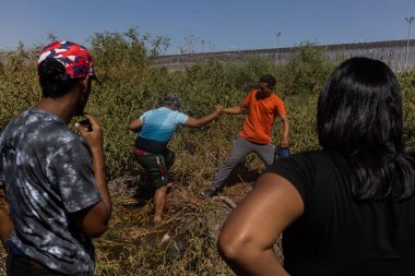 Ciudad Juarez sınırındaki yoğun bitki örtüsünde gezinen bireyler göç sorunlarını vurguluyor.