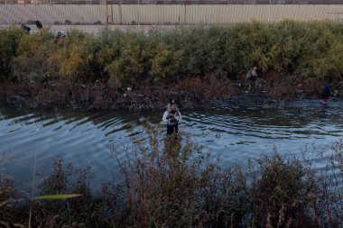 Göçmenler, Ciudad Juarez sınırından geçen bir nehri yüksek bariyerlerin arasından geçiyorlar..
