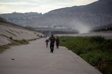 Bir aile, Ciudad Juarez sınırında bulutlu bir gökyüzünün altında, göçün acı gerçeklerini yansıtan bir yolda yürüyor..