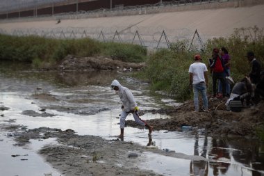 Siviller, sınır güvenliğinin gözetimi altında Ciudad Juarez sınırındaki çamurlu bir nehir kıyısında geziniyorlar..