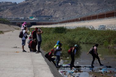 Göçmenler Ciudad Juarez yakınlarında, dikenli tellerle çevrili bir nehir yatağından geçiyorlar..