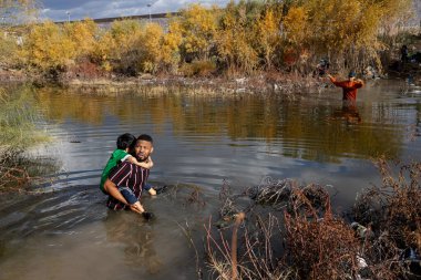 Bir adam çocuğu Ciudad Juarez sınırından karşıya, göçmenlerin güvenli bir yer bulmak için sık sık tehlikeli koşullarla karşı karşıya kaldıkları yere taşıyor..