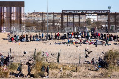 Göçmenler, Ciudad Juarez 'deki sınır duvarının yanında açık gökyüzünün altında, kişisel eşyalarla çevrili olarak toplandılar..