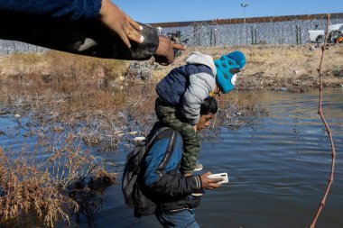 Bir adam çocuğu Rio Grande 'den karşıya Ciudad Juarez sınırında taşıyor. Göç sorunlarını vurguluyor..