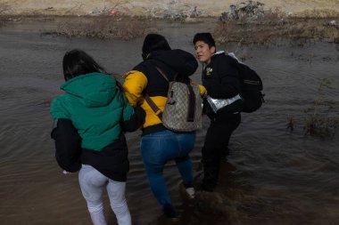 Ciudad Juarez 'deki göçmenler nehirden geçerek, birbirlerine eşyaları taşıyarak yardım ediyorlar..