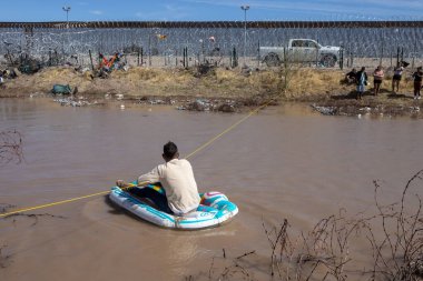 Göçmenler Ciudad Juarez sınırında şişme botla çamurlu bir nehirde yol alıyorlar..
