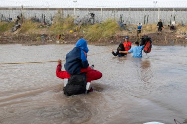 Göçmenler, düzensiz bir sınır geçişi sırasında Ciudad Juarez yakınlarındaki çamurlu bir Rio Grande 'de iple yol alıyorlar..