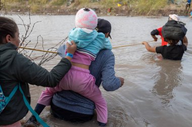 Göçmenler Rio Grande 'yi geçmek için bir ip kullanıyorlar. Ciudad Juarez yakınlarında, düzensiz bir sınır geçişi sırasında bir çocuk taşıyor..