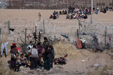 Yorgun göçmenler Rio Grande 'yi geçtikten sonra Ciudad Juarez' deki sınır duvarının yanında dinleniyorlar..