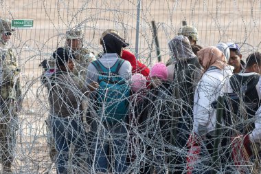 Aralarında ailelerin de bulunduğu göçmenler, güvenlik güçlerinin gözetiminde Ciudad Juarez 'deki sınır duvarının yanında toplandılar..