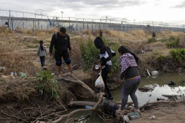 Çocuklar da dahil olmak üzere göçmenler, Rio Grande 'yi geçtikten sonra Ciudad Juarez' deki sınır duvarının yakınındaki zorlu arazide geziniyorlar..