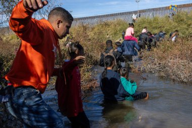 Çocuklar da dahil olmak üzere göçmenler, Ciudad Juarez 'deki sınır duvarının yakınındaki bir su yolundan geçerek bölgeden geçtiler..