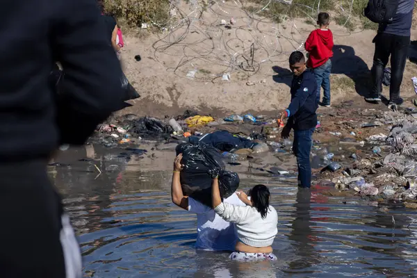 Bir kadın ve çocuk, bir sınır memurunun tetikte olduğu Ciudad Juarez sınırındaki sel sularında geziniyor..