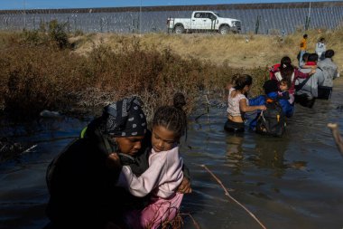 Çocuklar da dahil olmak üzere siviller, Ciudad Juarez 'deki bir güvenlik çiti yakınındaki sel sularında geziniyorlar..