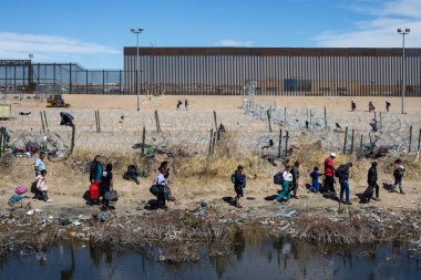 Çantalarla dolu siviller, açık gökyüzünün altındaki Ciudad Juarez sınır duvarında toplanın..