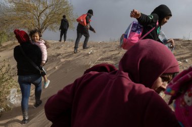 Çocuklar da dahil olmak üzere siviller, Ciudad Juarez yakınlarındaki kumlu bir araziden geçerek göç rotalarında yol alırken yanlarında eşyalar taşıyorlar..