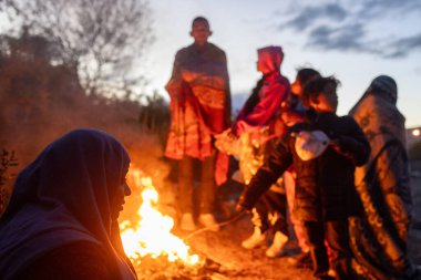 Çocuklar da dahil olmak üzere siviller, Ciudad Juarez yakınlarında alacakaranlıkta bir ateşin başında toplanarak göç sorunlarının ortasında ısınmak istiyorlar..