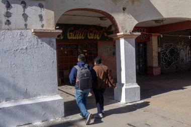 İki adam, canlı graffitilerle süslenmiş, kentsel bozulma ve esnekliği tasvir eden kepenkli bir kafede yürüyor..