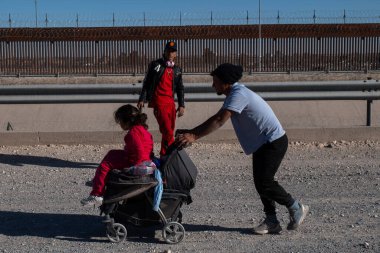 Ciudad Juarez 'de bir bebek arabasında bir çocuğa yardım eden bir adam, yüksek bir sınır çitinin yanında,.