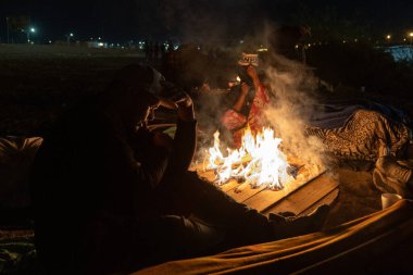 Ciudad Juarez yakınlarındaki bir kamp ateşinin etrafında, şehir ışıklarına bakan insanlar..