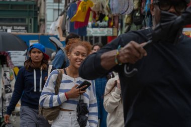 Bir kadın hareketli bir sokak pazarında gezinirken neşeyle ışıldıyor, şehir hayatının coşkulu ruhunu yansıtıyor..